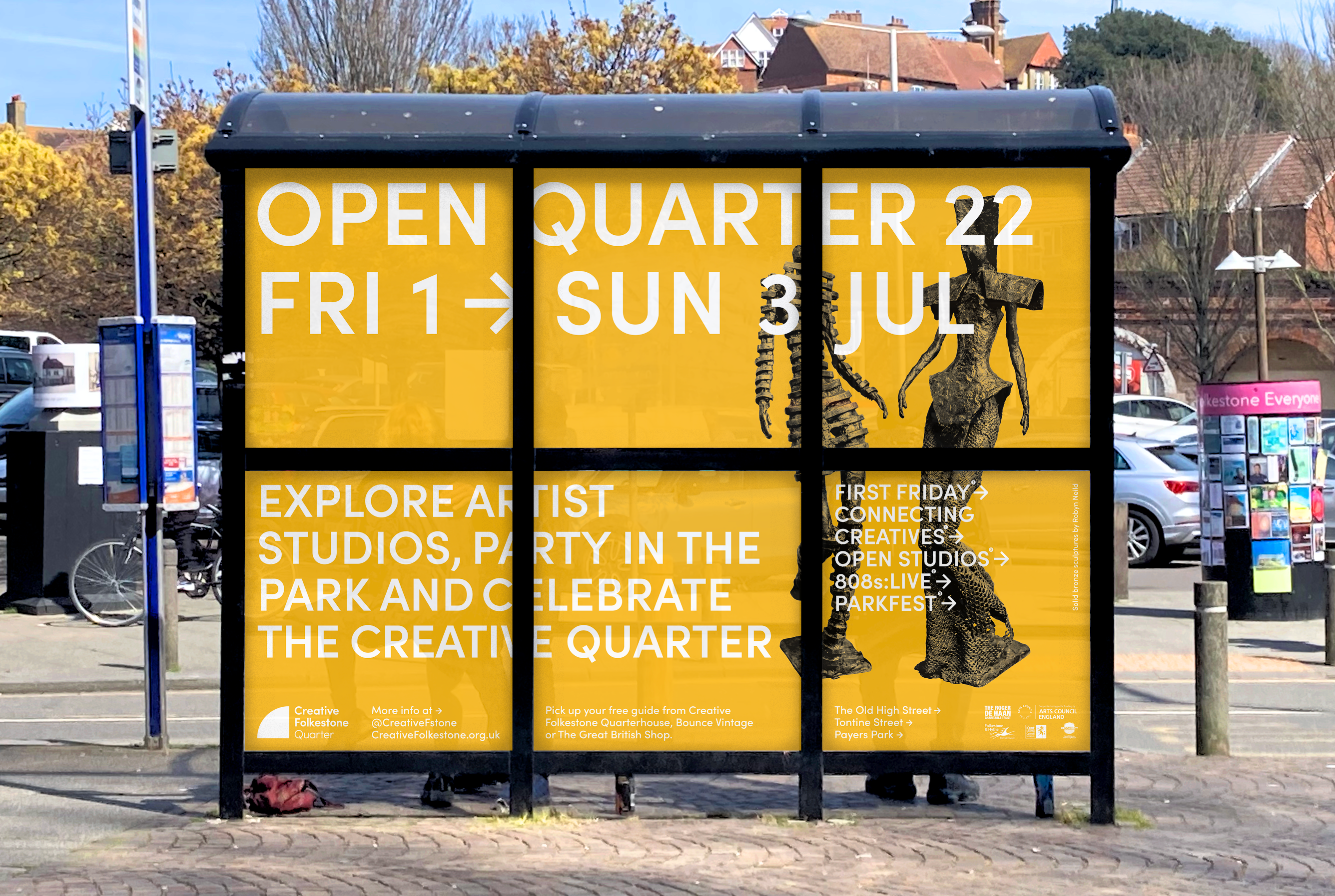 Open Quarter 22 posters in a bus shelter: yellow panels with large white type and two bronze sculptures